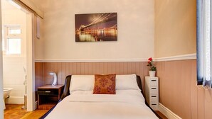A hotel room with a large bed, a nightstand, a bedside table, a wall-mounted lamp, a potted plant, and a framed picture of a bridge. - Thistle Dhu Guest House (Blackpool)