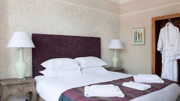A neatly made bed with white linens, two bedside lamps, a plaid throw blanket, and a white robe hanging on a door.
