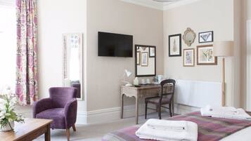 Un dormitorio con cama, escritorio, silla, televisión y cuadros en la pared.