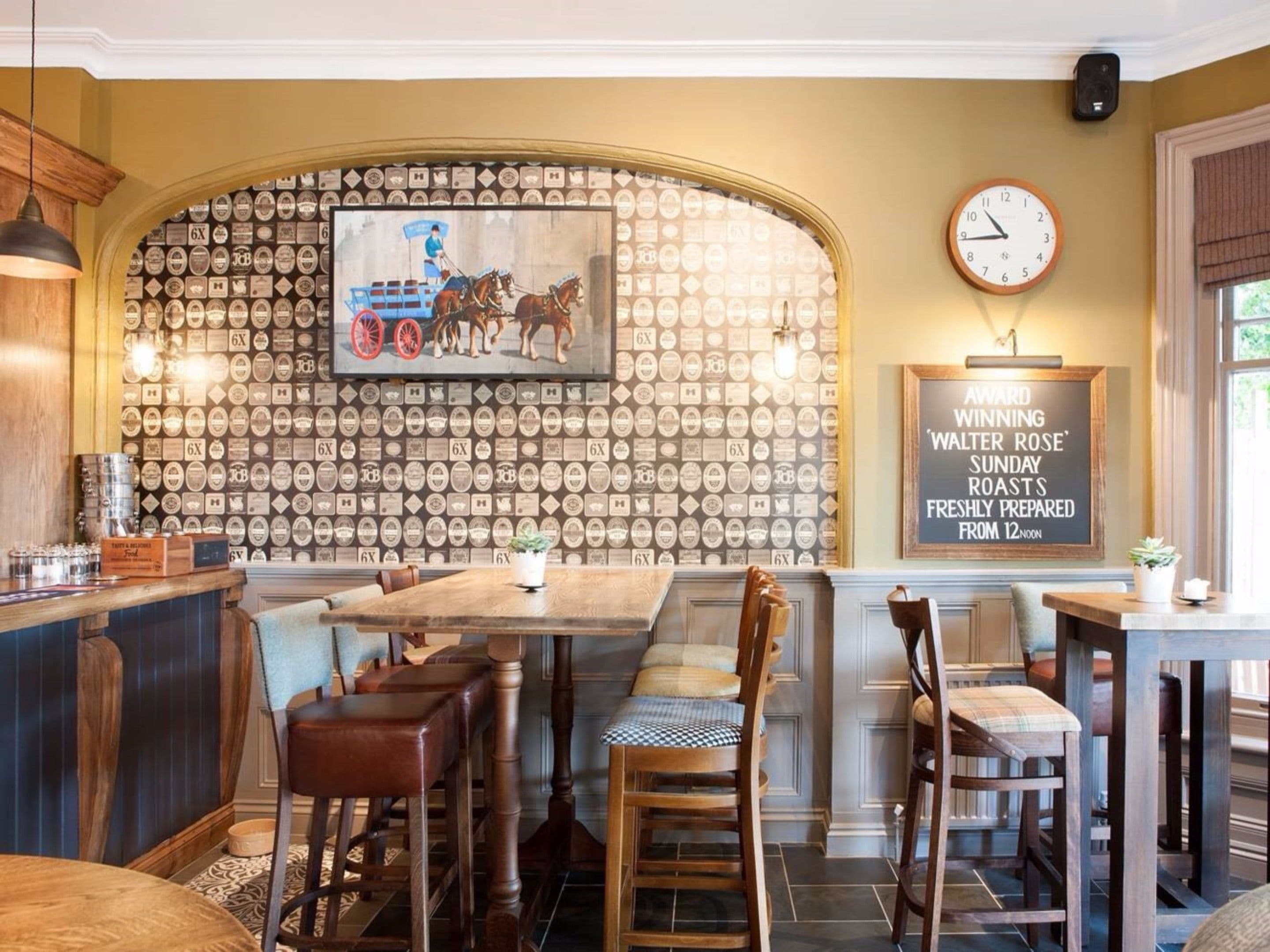 A restaurant interior with a wall of beer labels, a clock, and a chalkboard sign advertising Sunday roasts.