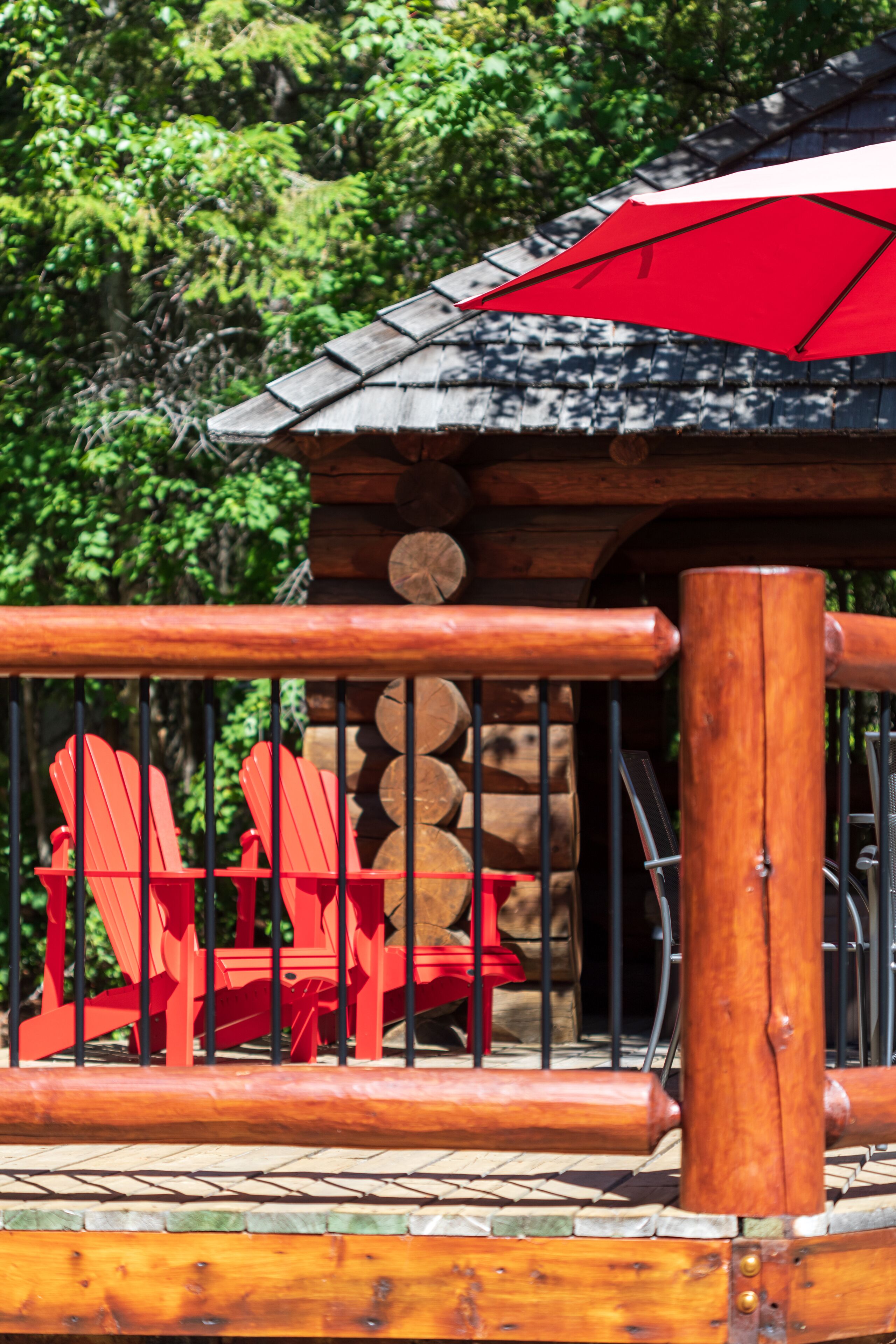 A wooden deck with a metal railing, red Adirondack chairs, and a red umbrella.