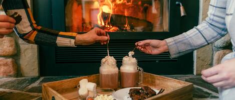 A wooden tray with drinks, snacks, and a plate of food in front of a fireplace.