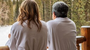 Two people in white robes standing by a wooden railing, overlooking a snowy mountain and dense forest. - Moberly Lodge (Golden)