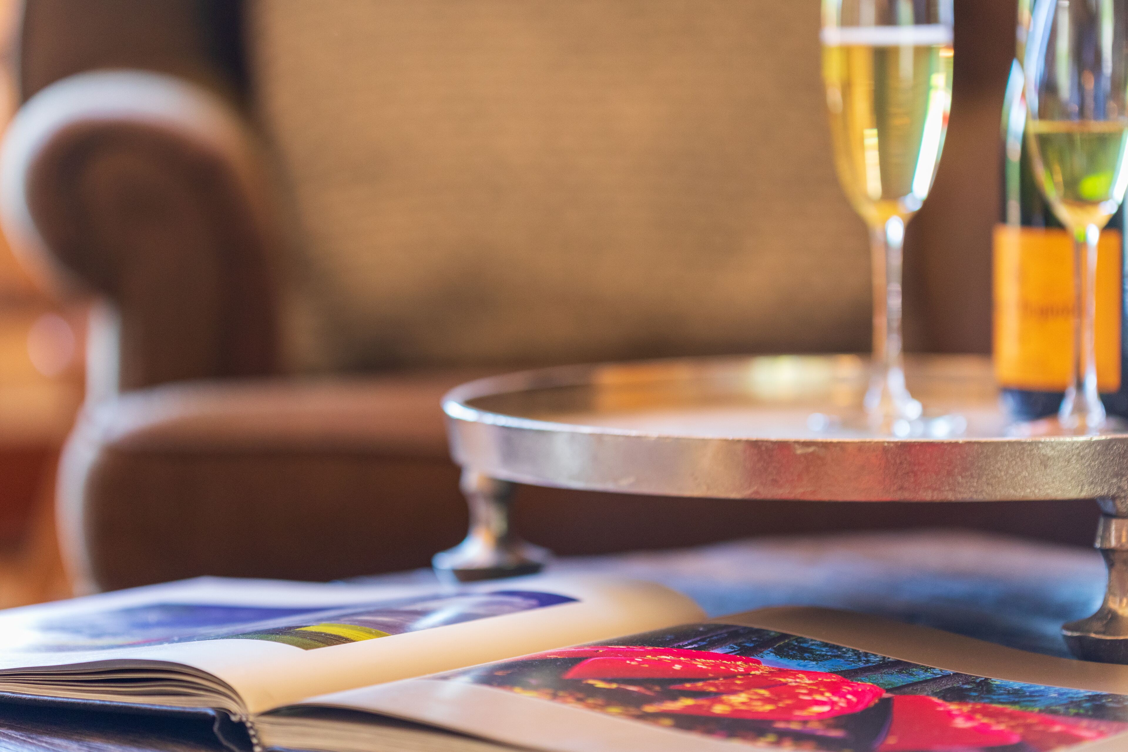 A close-up of a magazine with colorful pages, a metal tray with a glass of champagne, and a bottle of wine.