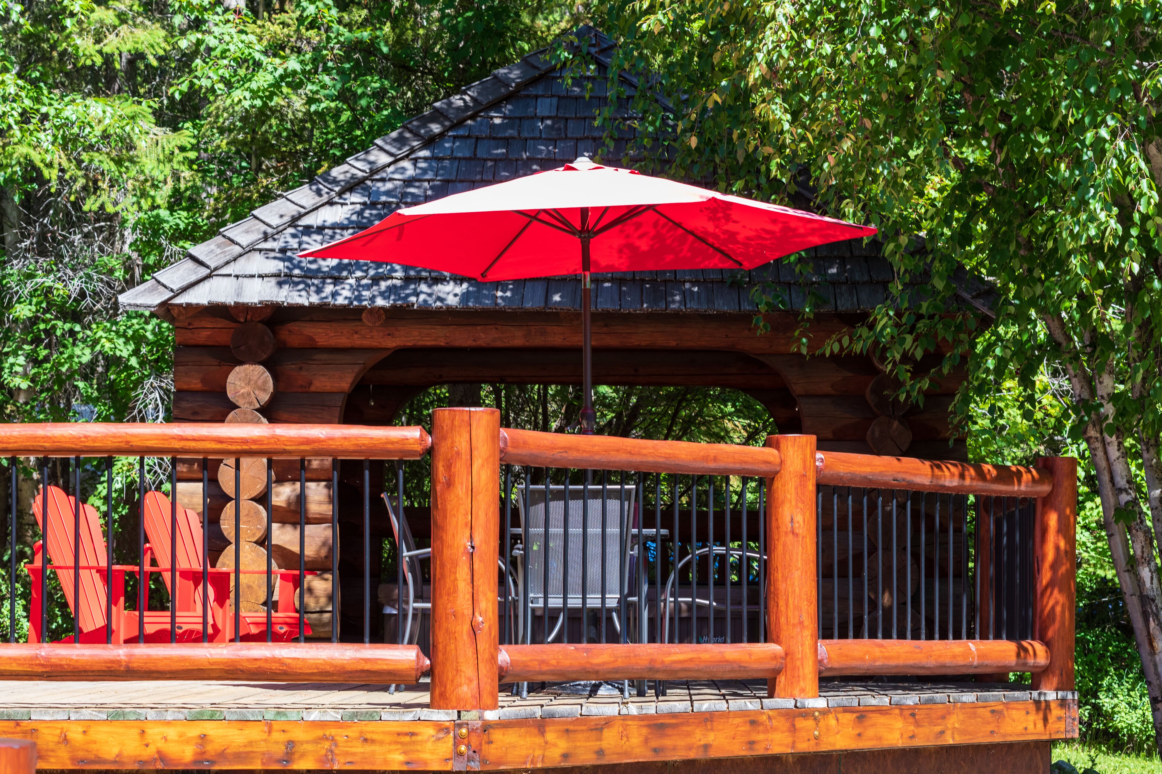 A wooden deck with a red umbrella, wooden chairs, and a metal fence.
