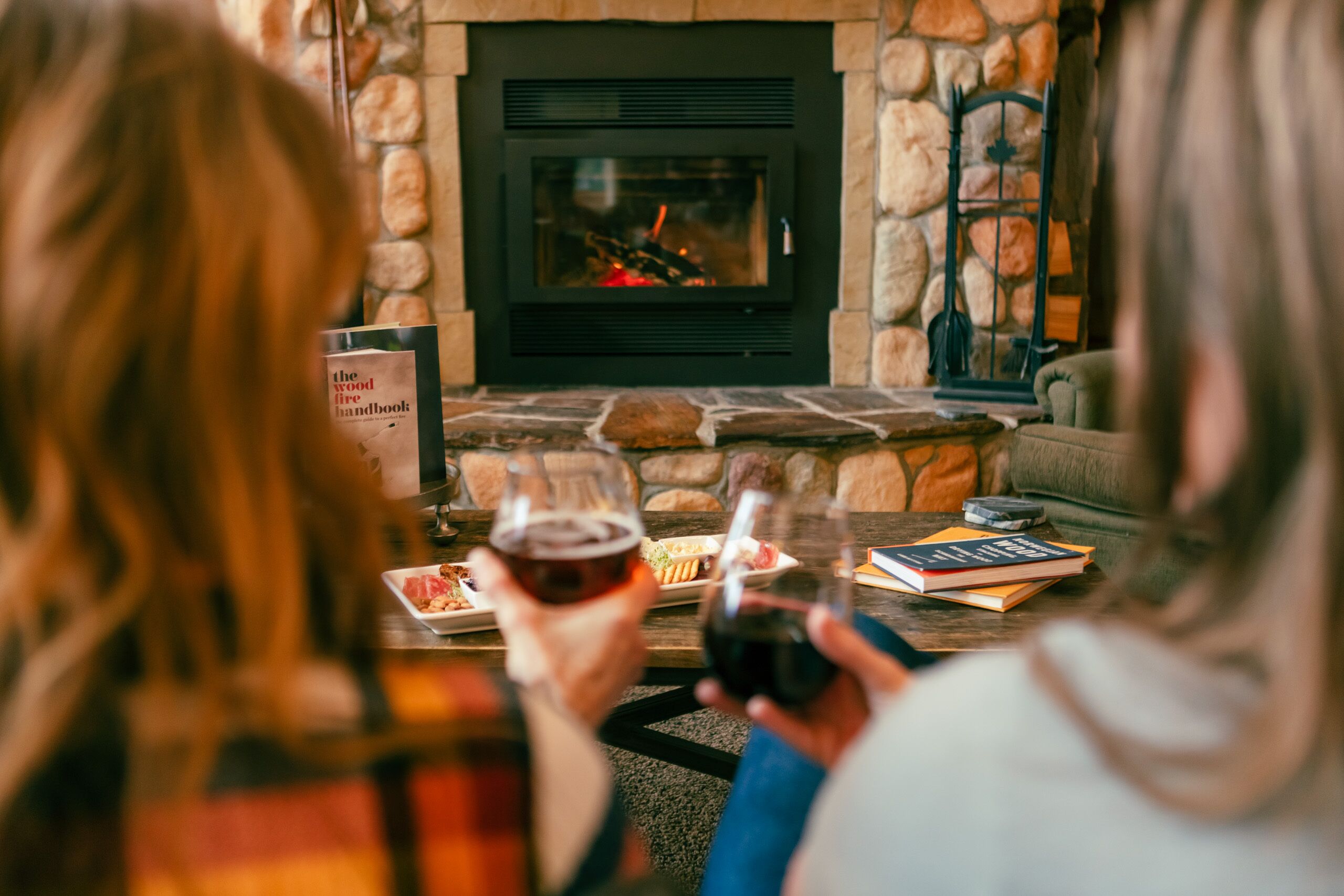 Una chimenea de piedra con fuego, un libro y una copa de vino sobre una mesa.