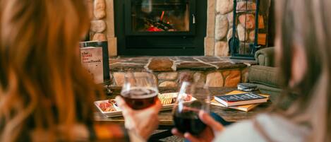 Una chimenea de piedra con fuego, un libro y una copa de vino sobre una mesa.