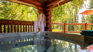 A wooden cabin with a hot tub, wooden railings, and a view of trees. - Moberly Lodge (Golden)