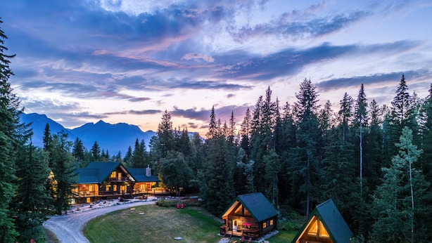 A lodge with multiple cabins surrounded by a forest and mountains in the background. - Moberly Lodge (Golden)