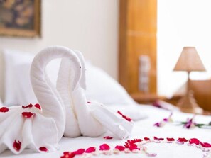 A bed with a swan-shaped towel and scattered rose petals.