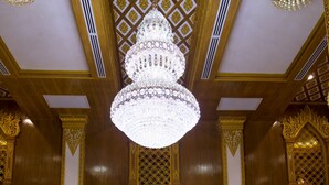 A grand hall with a large chandelier, ornate golden columns, and red drapes.