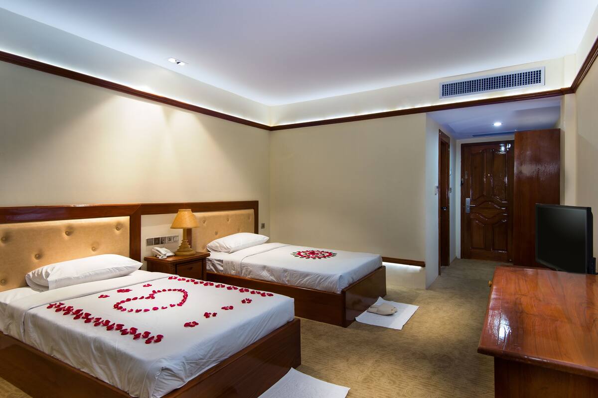A hotel room with two beds, a wooden desk, a television, and a door leading to another room.
