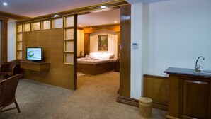 A hotel room with a bed, a television, a desk with a sink, and a wicker basket.
