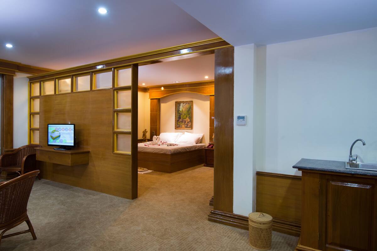 A hotel room with a bed, a television, a desk with a sink, and a wicker basket.