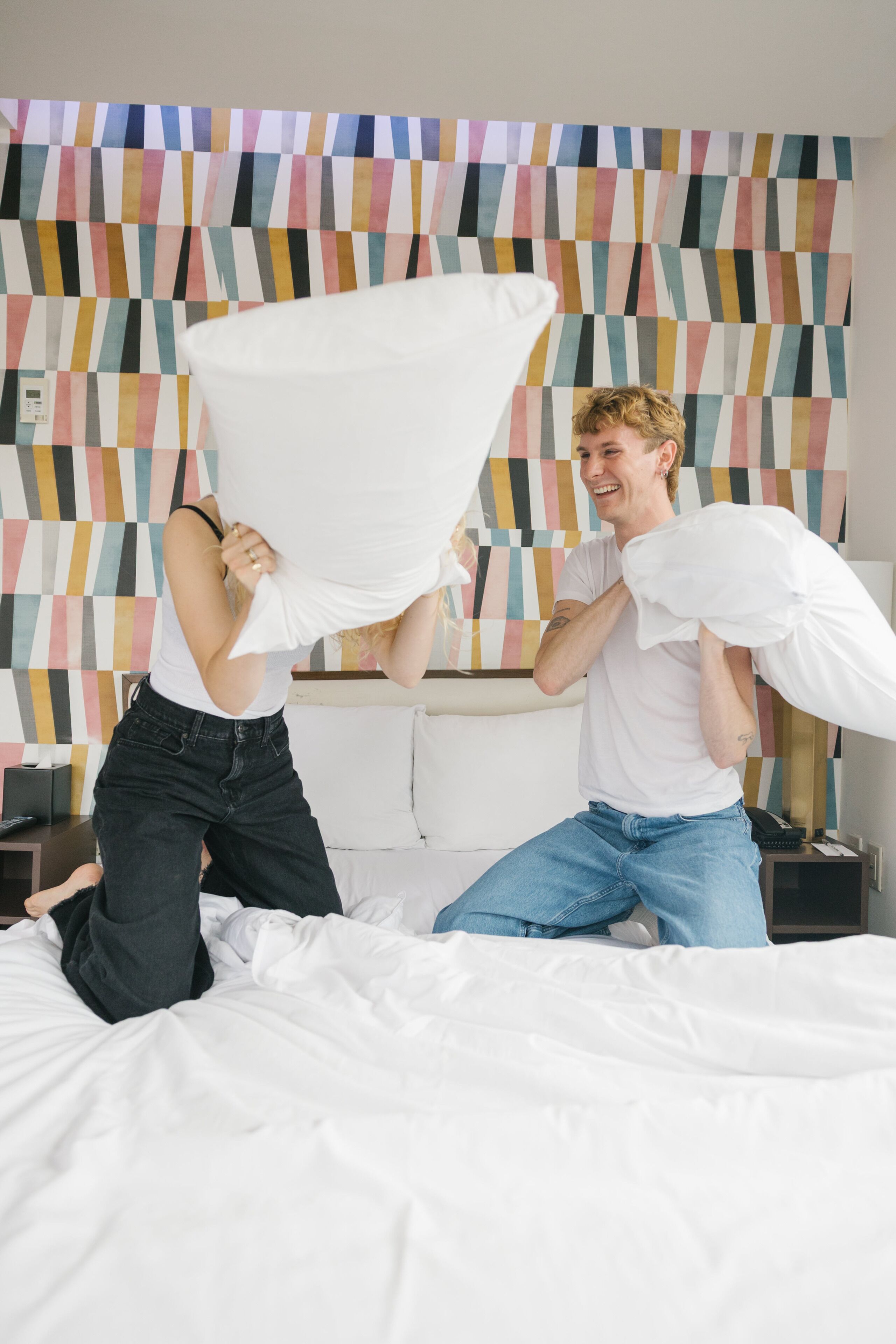 Una cama con ropa blanca en una habitación con pared de estampado geométrico colorido.