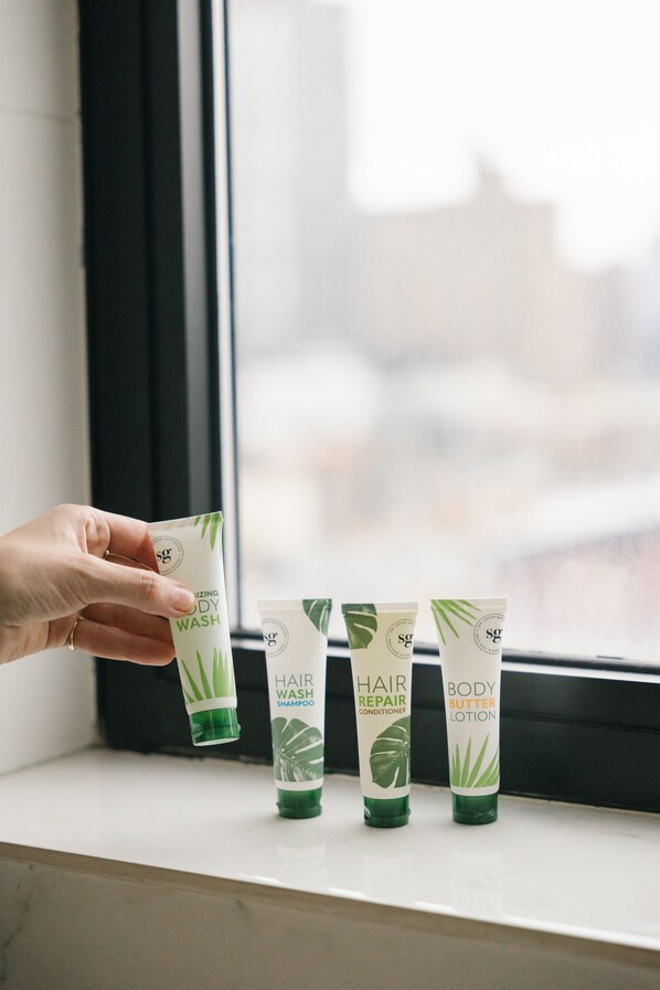 A hand holding a tube of body wash next to three other tubes of hair care products on a windowsill. - Orchard Street Hotel (New York)