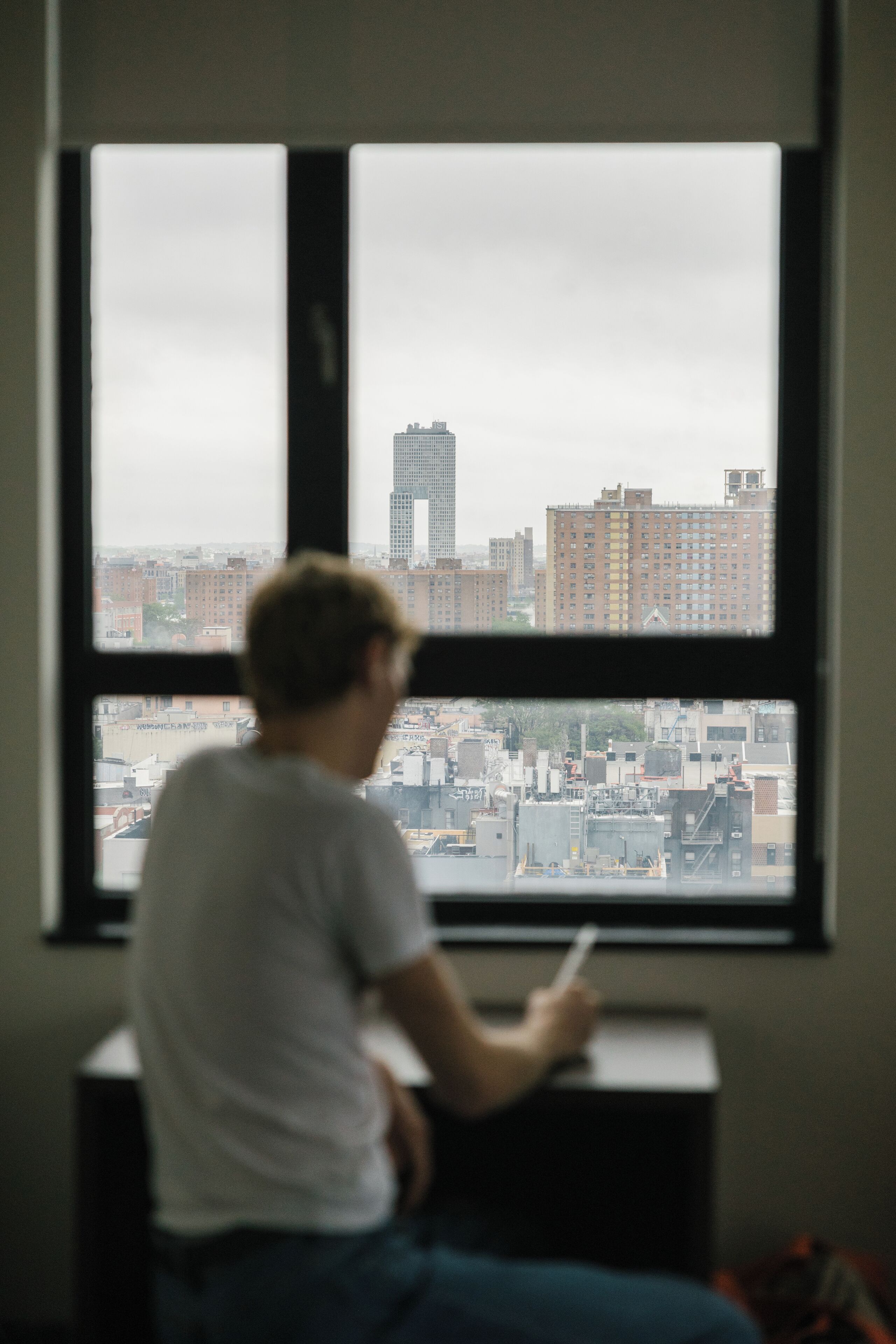Une personne assise à un bureau près d’une fenêtre donnant sur un paysage urbain.