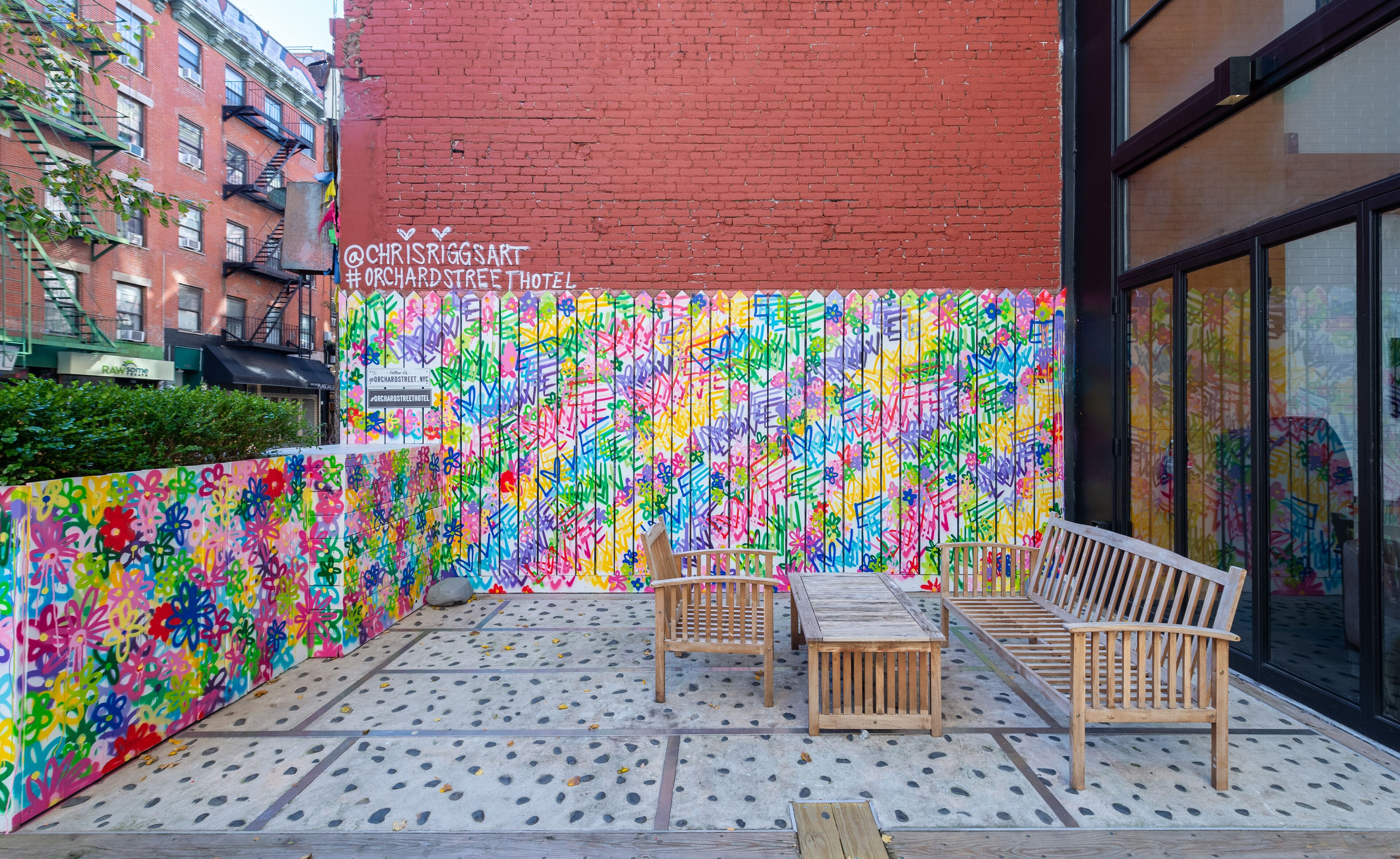 An outdoor seating area with a colorful graffiti wall, wooden benches, and a tiled floor.