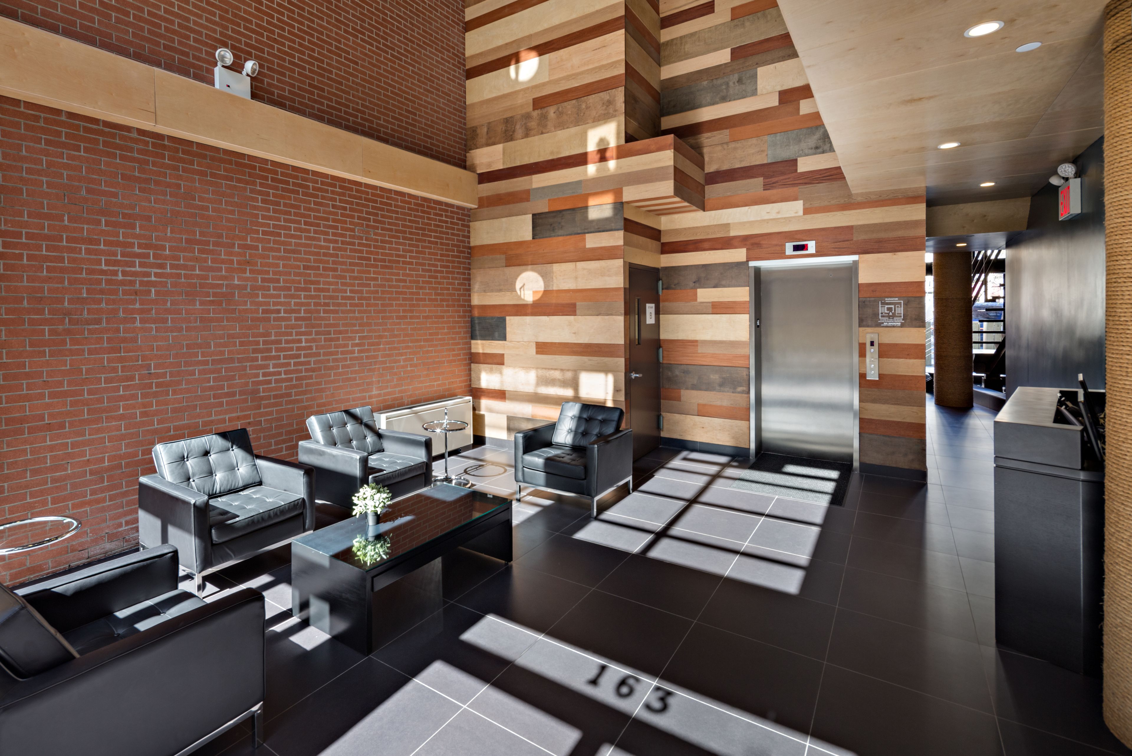 A modern lobby with a brick wall, a reception desk, and a seating area with sofas and a coffee table.