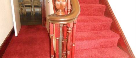 A staircase with a red carpet leading to a room with a dining area visible in the background.