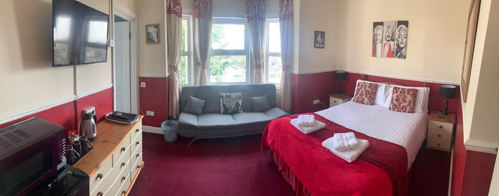 A bedroom with a bed, a sofa, a TV, a dresser, and a window with curtains.