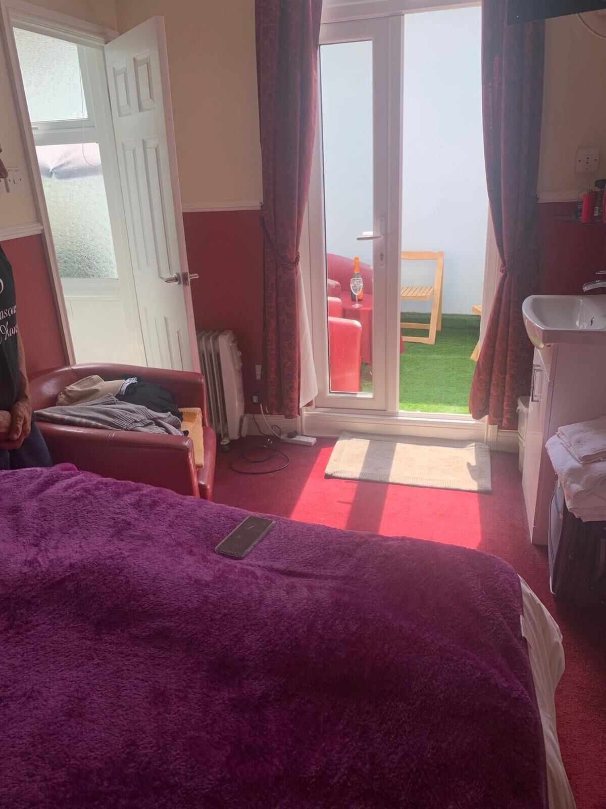 A room with a bed, a small table, a chair, a window with curtains, and a view of the outside.
