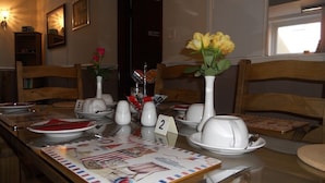 A dining table set with numbered place settings, a vase with yellow flowers, and a table runner with a vintage design. - All Seasons Guest House (Great Yarmouth)