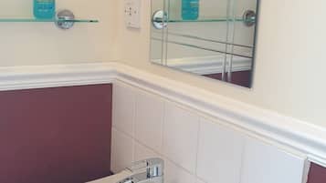 Un baño con lavamanos blanco, un espejo y dos botellas de jabón en un estante de vidrio.