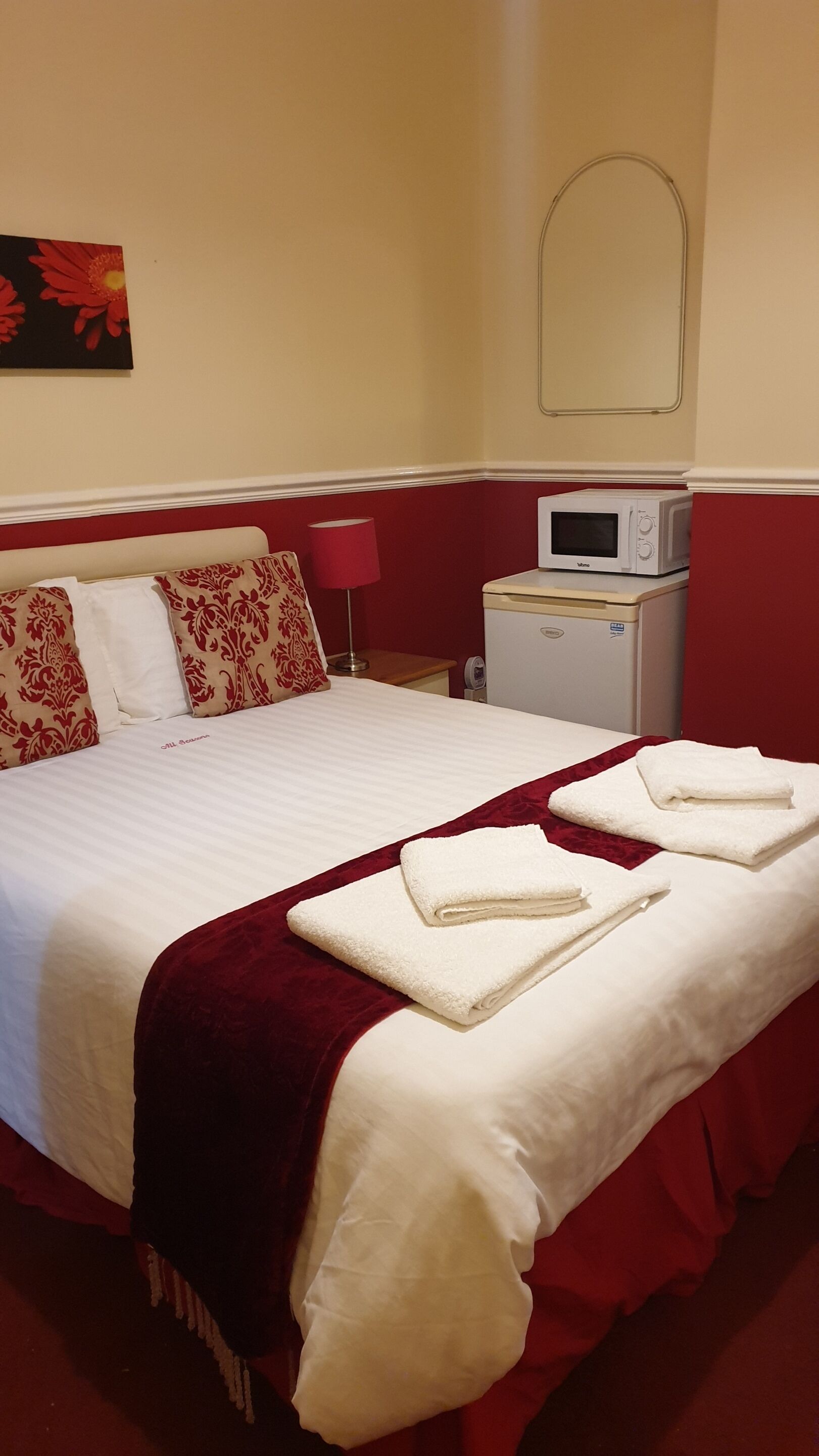 A hotel room with a large bed, a bedside table with a lamp, a microwave, and a painting on the wall.