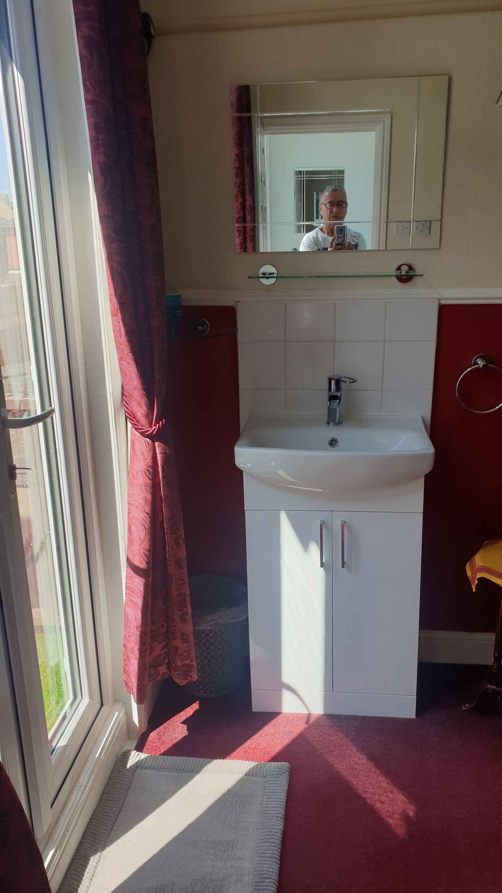 A bathroom with a white sink, a mirror above it, and a red towel rack.