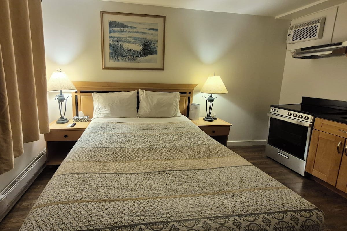 Habitación de hotel con una cama grande, dos lámparas de noche, un cuadro en la pared, una estufa y una ventana con cortinas.