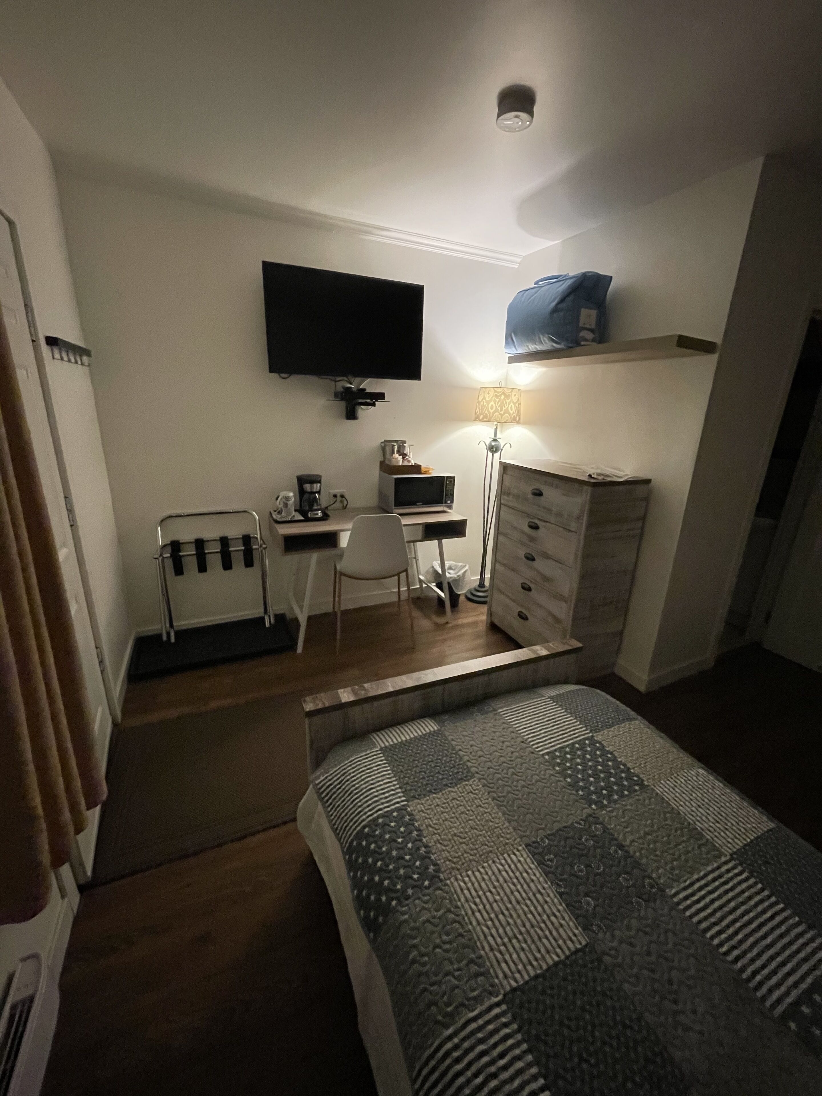 Une chambre d’hôtel comprenant un lit, un bureau avec une chaise, une télévision, une lampe et une commode.