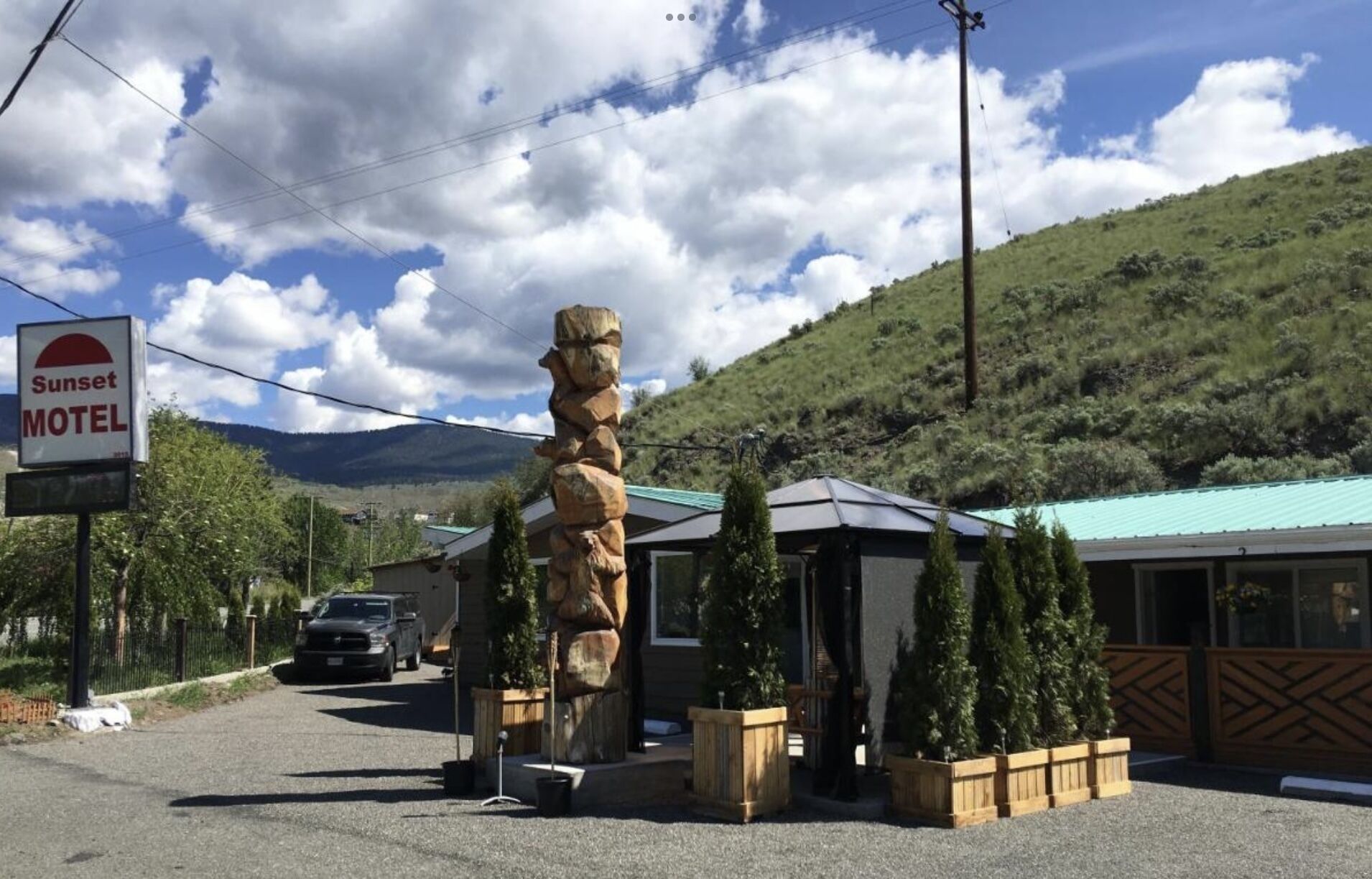 A motel with a stone sculpture, a sign reading "Sunset Motel," and a mountain in the background.