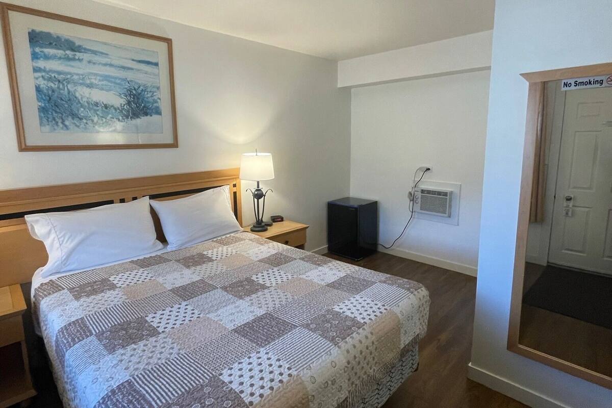 Una cama bien hecha con un edredón estampado, una lámpara de noche, una mesita y un televisor montado en la pared.