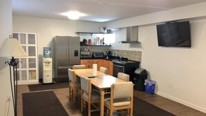 A compact kitchen with a dining area, a water dispenser, a refrigerator, a microwave, and a TV mounted on the wall. - Sunset Motel (Cache Creek)