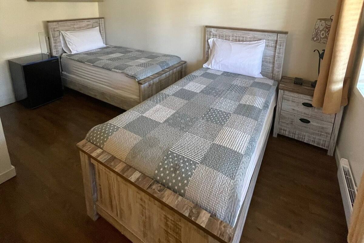 Un dormitorio con dos camas, una mesita de noche pequeña, una repisa y un bolso en una estantería.