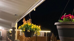A parking area with a row of cars, a covered walkway, and hanging flower planters. - Sunset Motel (Cache Creek)
