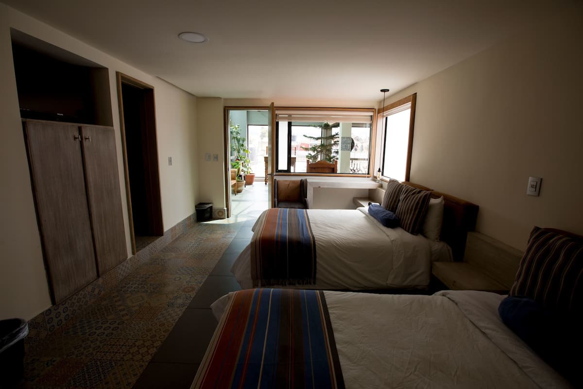 A hotel room with two beds, a sofa, a window with a view of the outside, and a door leading to a balcony.