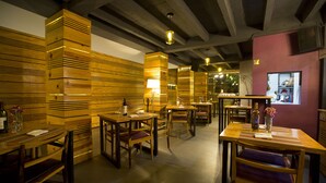 A restaurant interior with wooden panel walls, multiple tables and chairs, and hanging pendant lights.