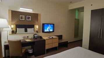 A hotel room with a bed, desk, chair, television, and wardrobe.
