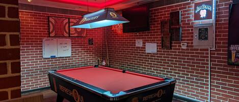 A pool table in a room with brick walls, a neon sign, and a mounted TV.