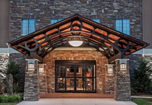 Un bâtiment doté d’une façade en pierre, d’un auvent d’entrée en bois et d’une grande porte vitrée.