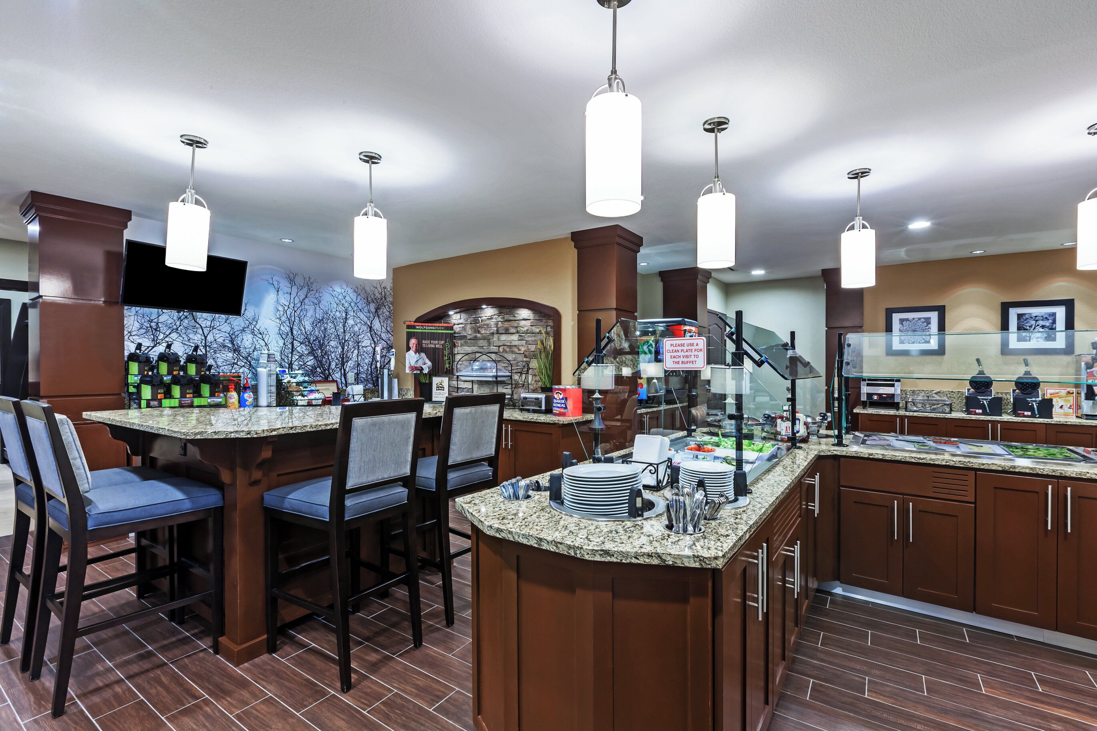Zona de bar en un hotel, con encimeras de granito, taburetes y una mesa de buffet.