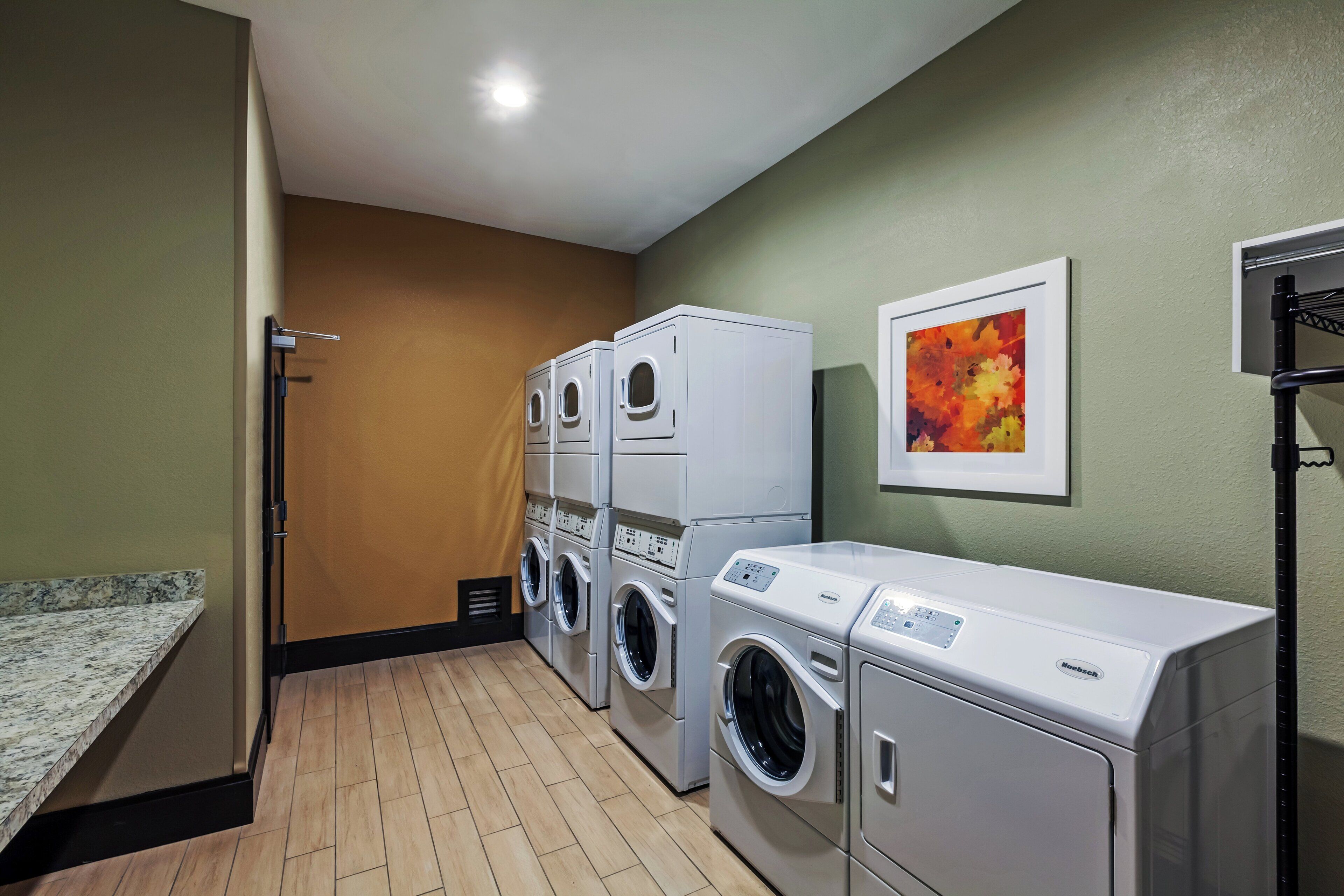 A laundry room with stacked washers and dryers, a wooden floor, and a green wall.
