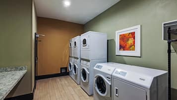 A laundry room with stacked washers and dryers, a wooden floor, and a green wall.
