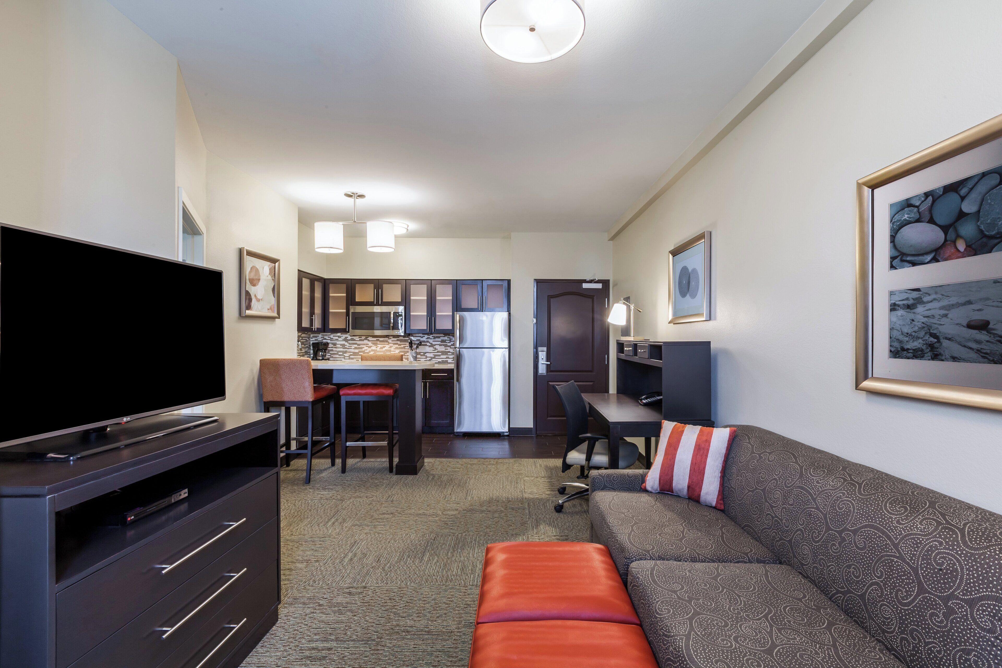 A modern hotel room with a flat-screen TV, a sofa, a dining area, and a kitchen.