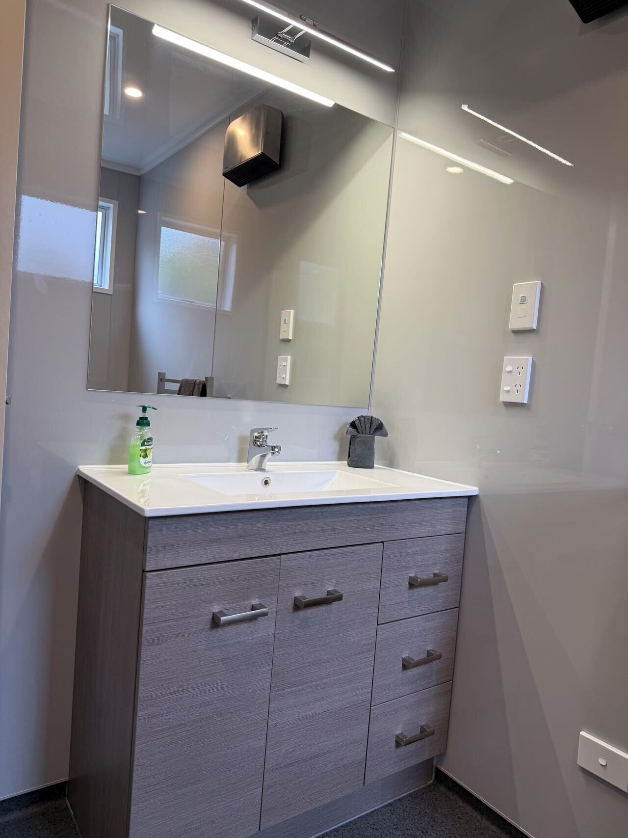 A modern bathroom with a large mirror, a white sink, and a wooden vanity with drawers.