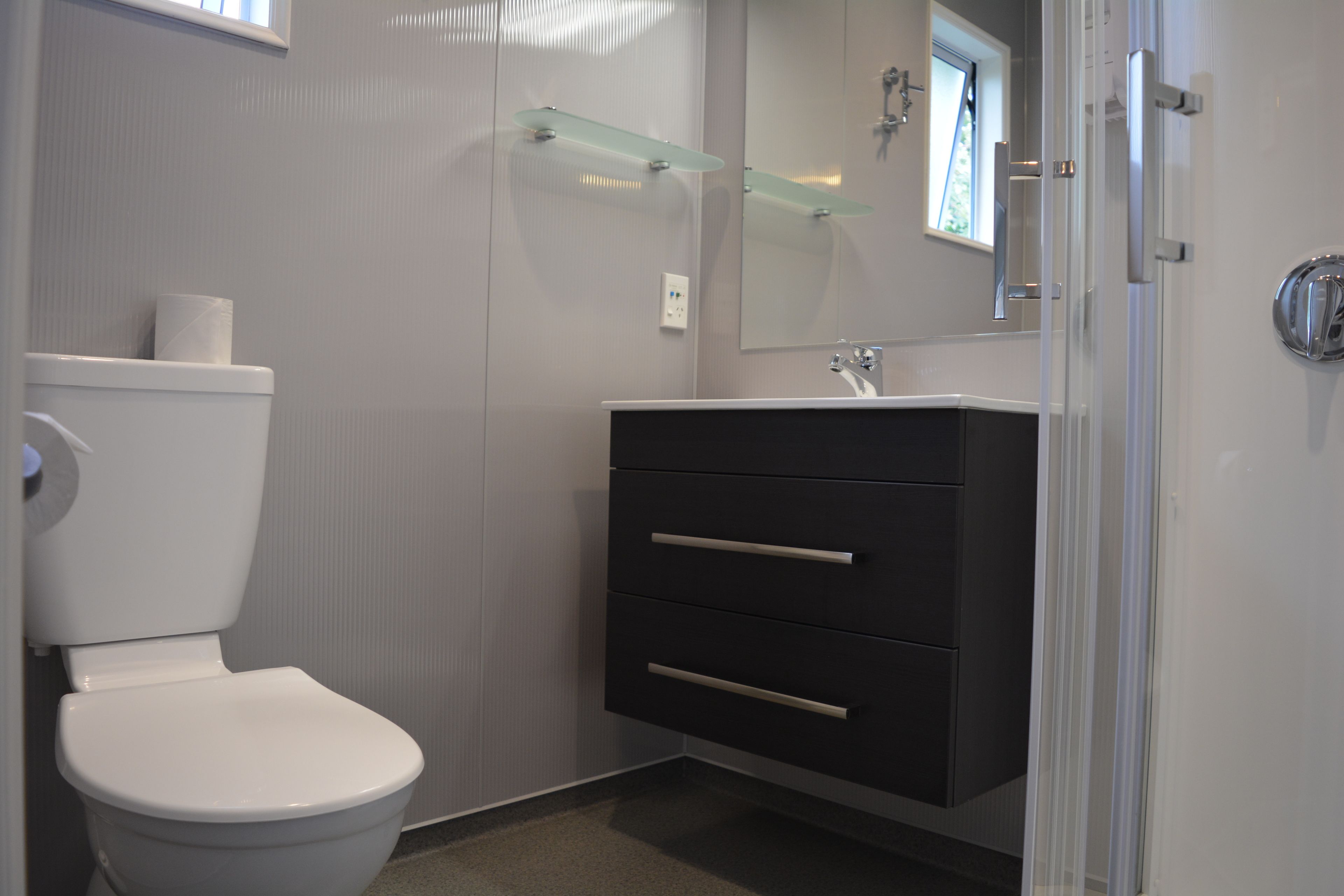 A modern bathroom with a toilet, a vanity with drawers, a glass shelf, and a mirror.