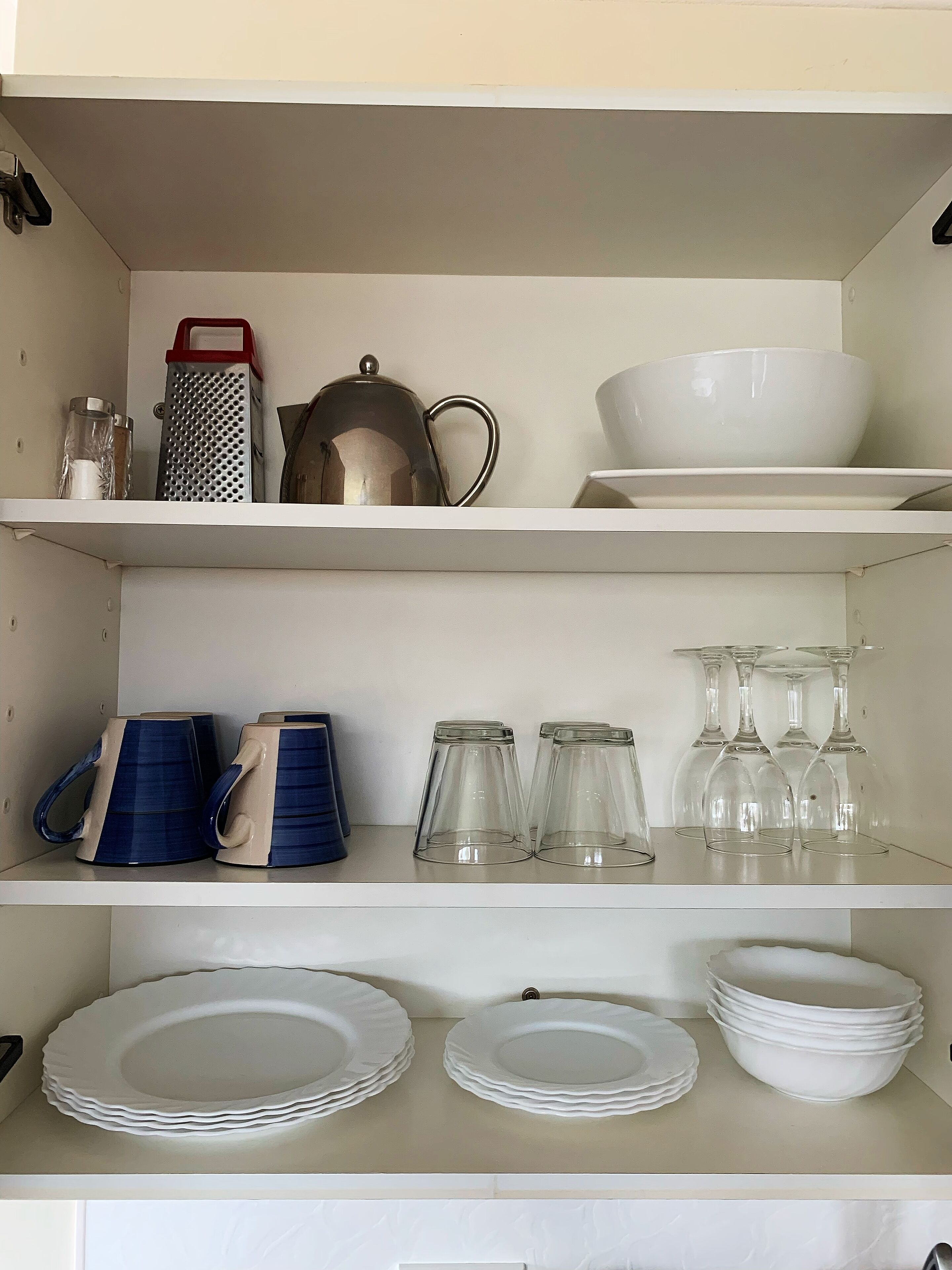 A kitchen shelf with a kettle, grater, and bowls.