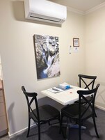 A room with a white air conditioning unit, a painting of a waterfall, a table with a tissue box, and two black chairs.